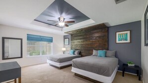 Een slaapkamer met twee bedden, een plafondventilator, een raam met blauwe jaloezieën en een houten accentmuur.