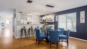 Een moderne keuken met witte kastjes, een bar met krukken en een eettafel met blauwe stoelen.