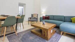 A modern living room with a wooden coffee table, green chairs, a blue sofa, and a red pillow.