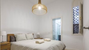 A bedroom with a bed, bedside lamps, a wooden nightstand, a window with a view, and a hanging light fixture.