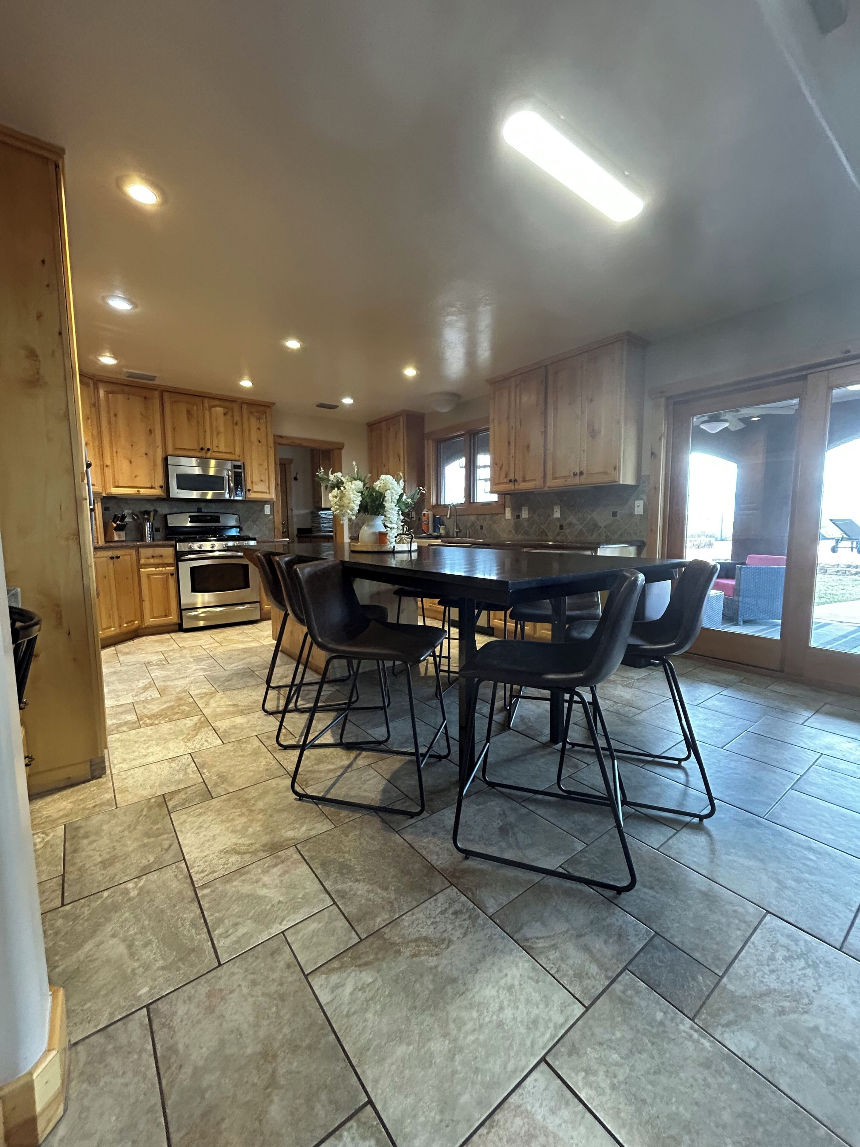 A modern kitchen with wooden cabinets, a central island, and a dining area with black chairs.
