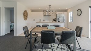 Et moderne køkken med hvide skabe, en central ø og et spiseområde med et træbord og sorte stole.