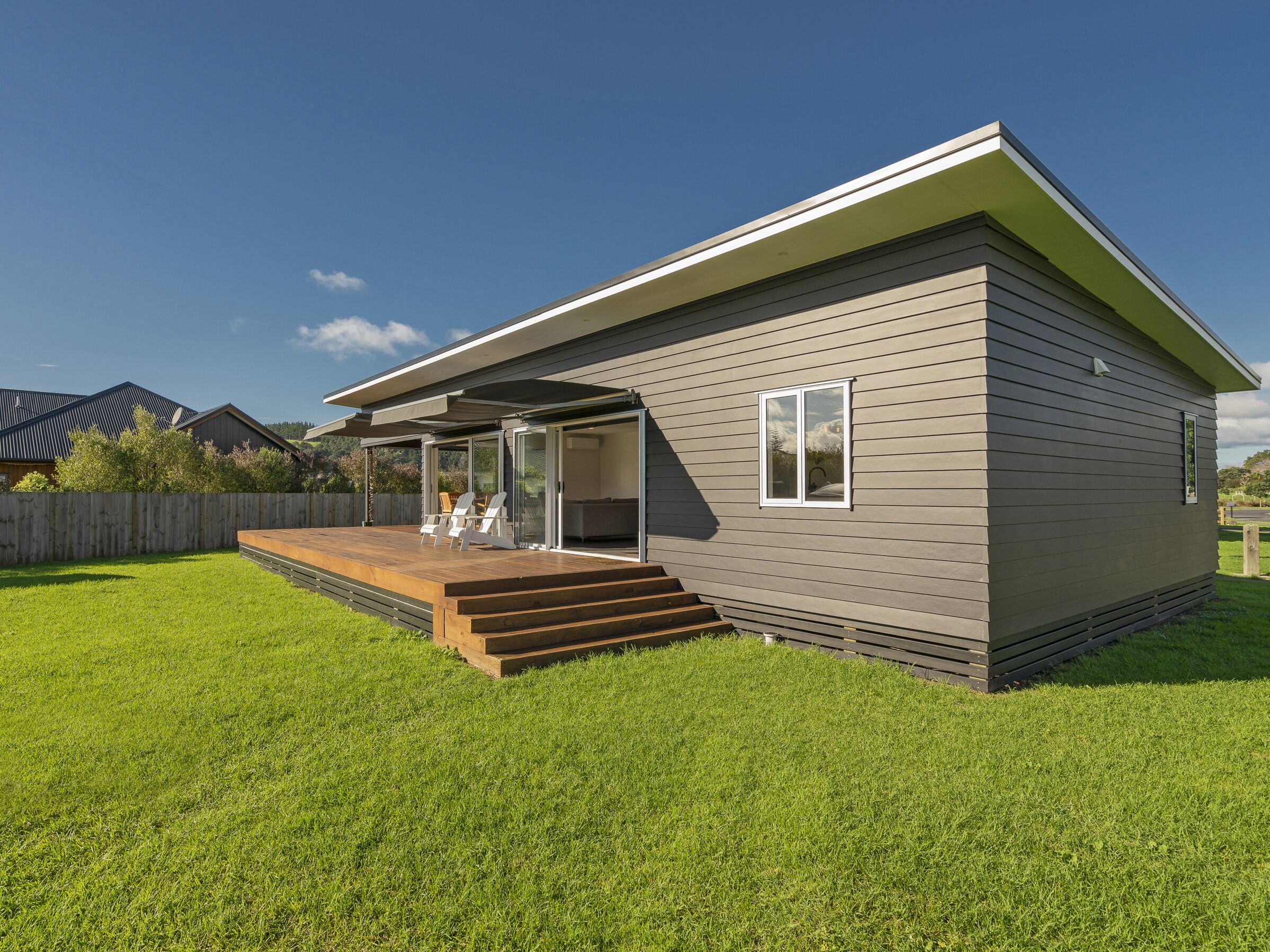 A modern single-story house with a covered patio, a wooden deck, and a well-maintained lawn.