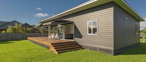 A modern single-story house with a covered patio, a wooden deck, and a well-maintained lawn.
