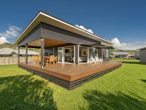 A modern house with a covered patio, a dining area, and a large sliding glass door leading to an outdoor kitchen. - Sundaze Escape - Cooks Beach Holiday Home (Cooks Beach)