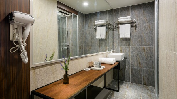 A modern bathroom with a wooden vanity, a glass shower enclosure, and a hairdryer mounted on the wall.