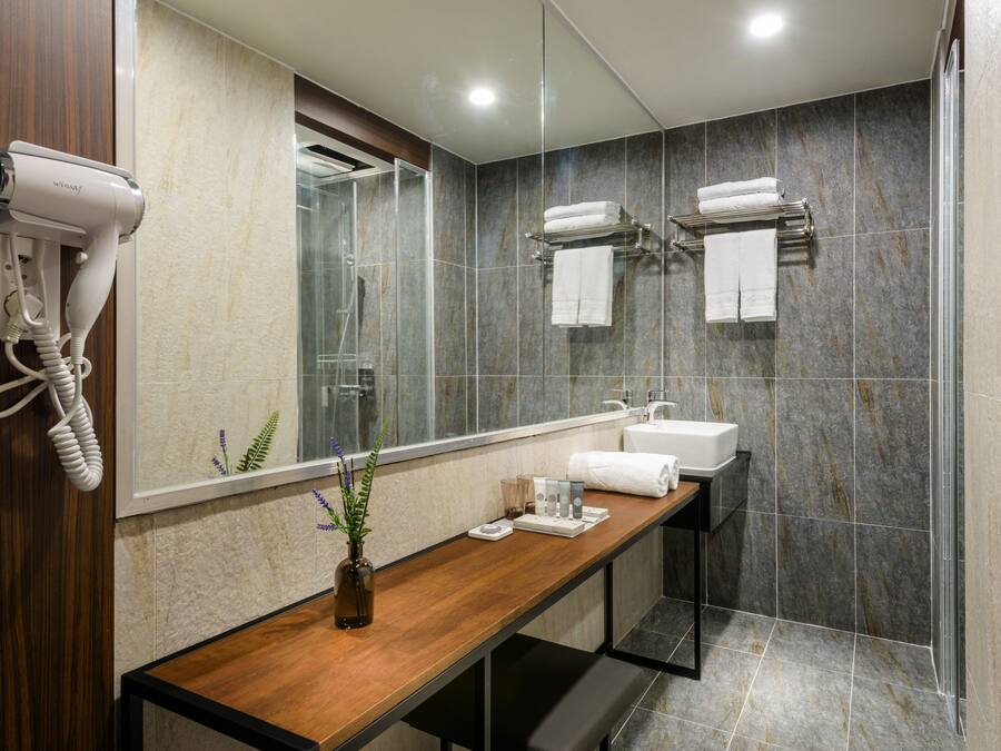 A modern bathroom with a wooden vanity, a glass shower enclosure, and a hairdryer mounted on the wall.
