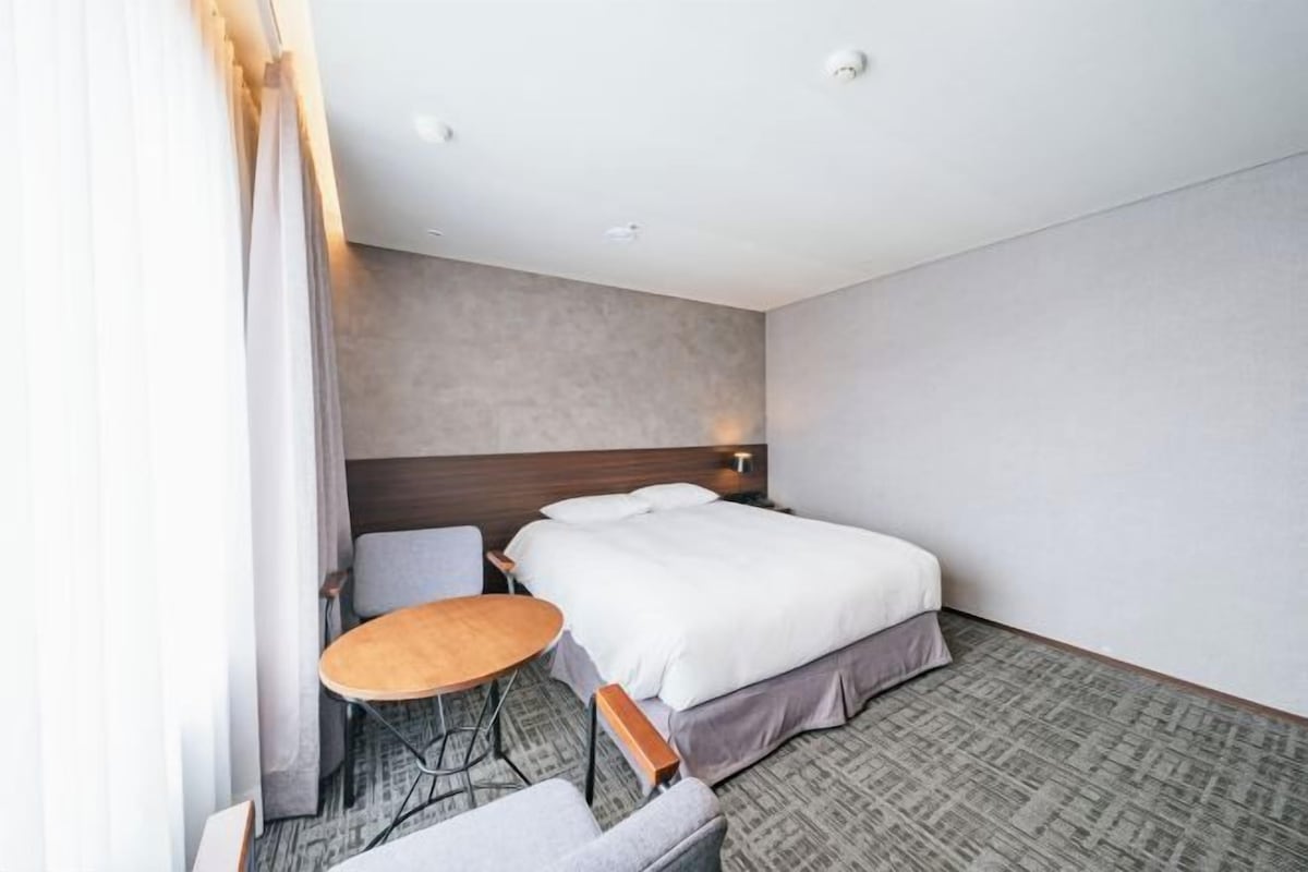 A hotel room with a bed, a small round table, a chair, and a sofa.