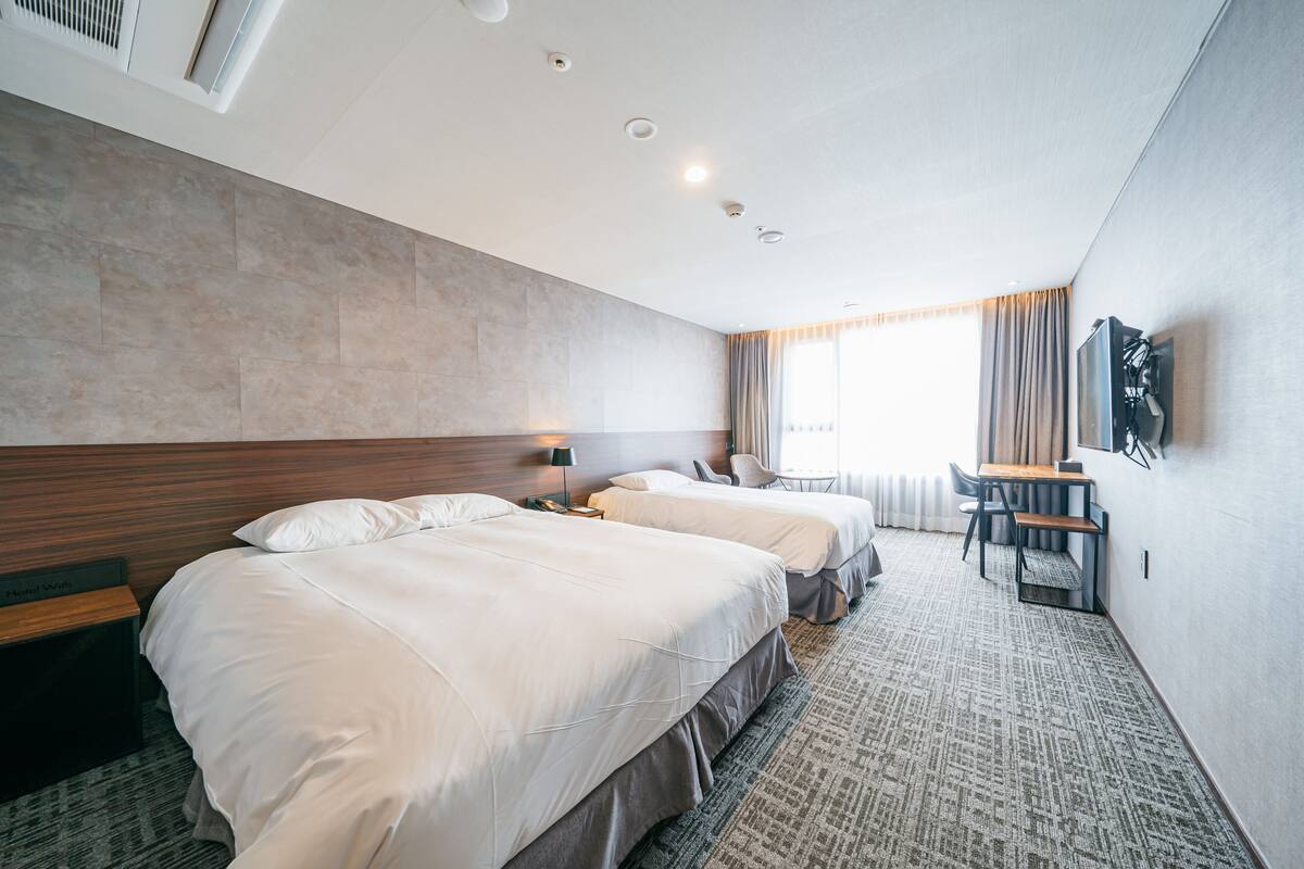 A hotel room with two beds, a desk, a chair, and a TV on the wall.