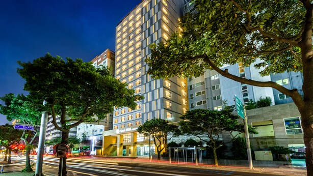 Un hôtel moderne doté d’une entrée imposante, de grandes fenêtres et d’une façade bien éclairée.