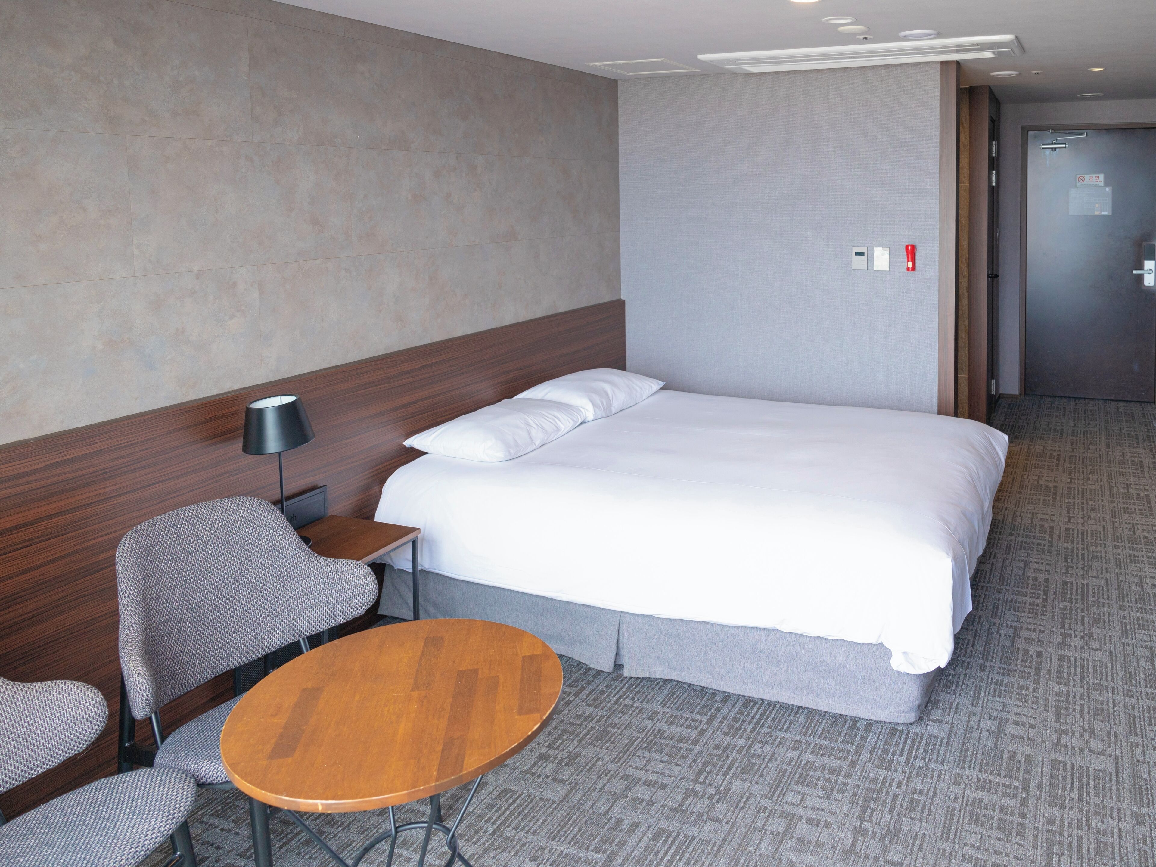 Une chambre d’hôtel avec un grand lit, une petite table, une chaise et une lampe.