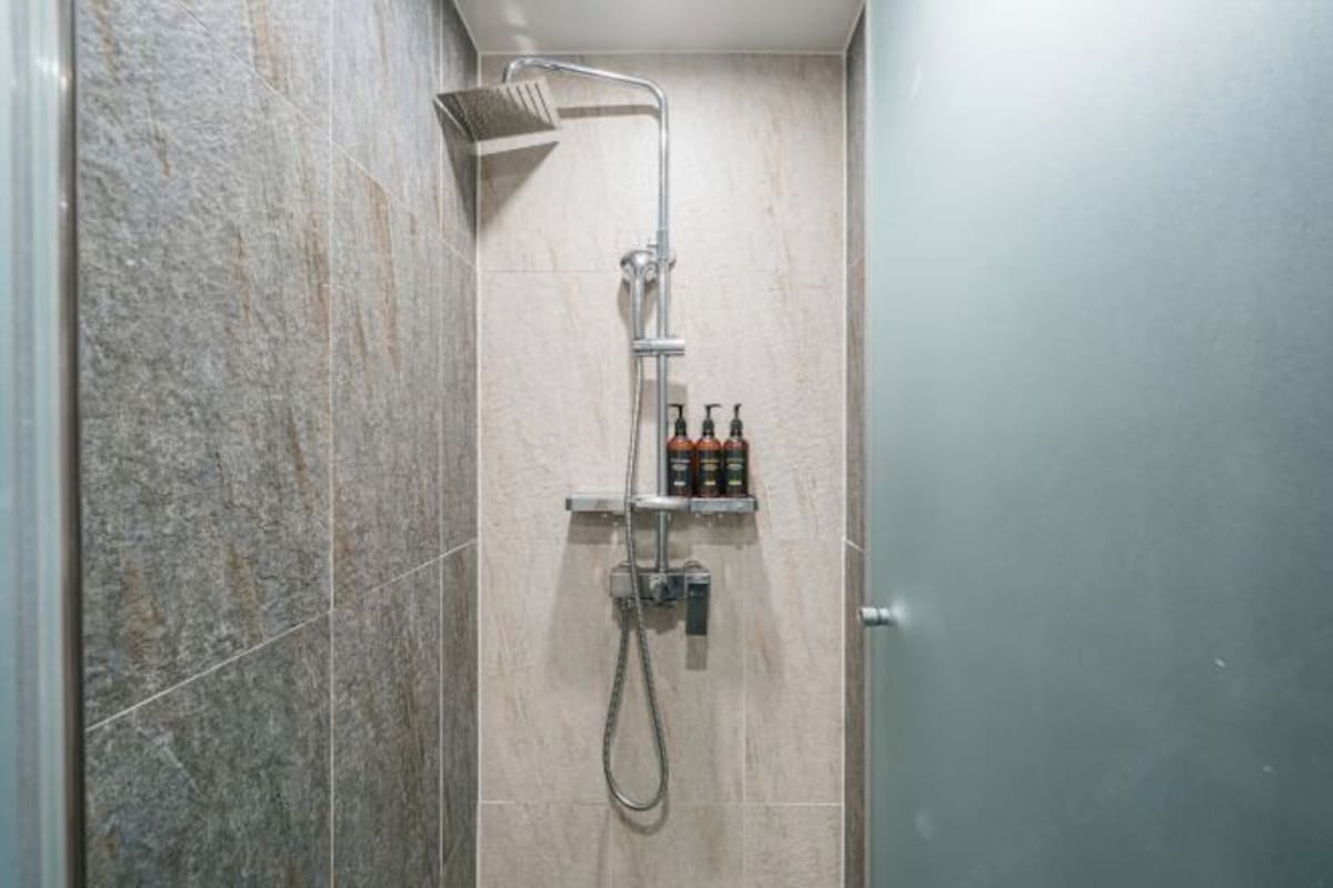 A shower with a handheld showerhead, a wall-mounted faucet, and a shelf with toiletries.