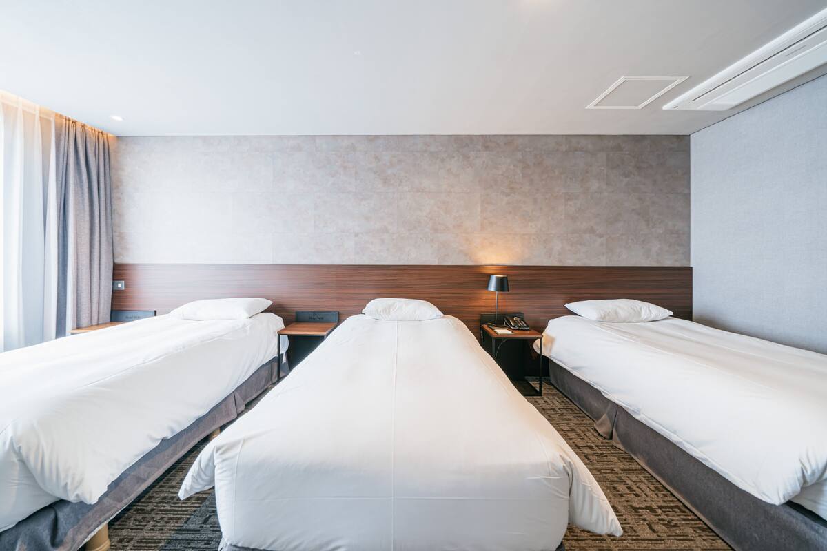 A hotel room with two single beds, a wooden headboard, a nightstand with a lamp, and a telephone.