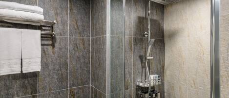 A modern bathroom with a glass-enclosed shower, marble tiles, and a towel rack with folded towels.