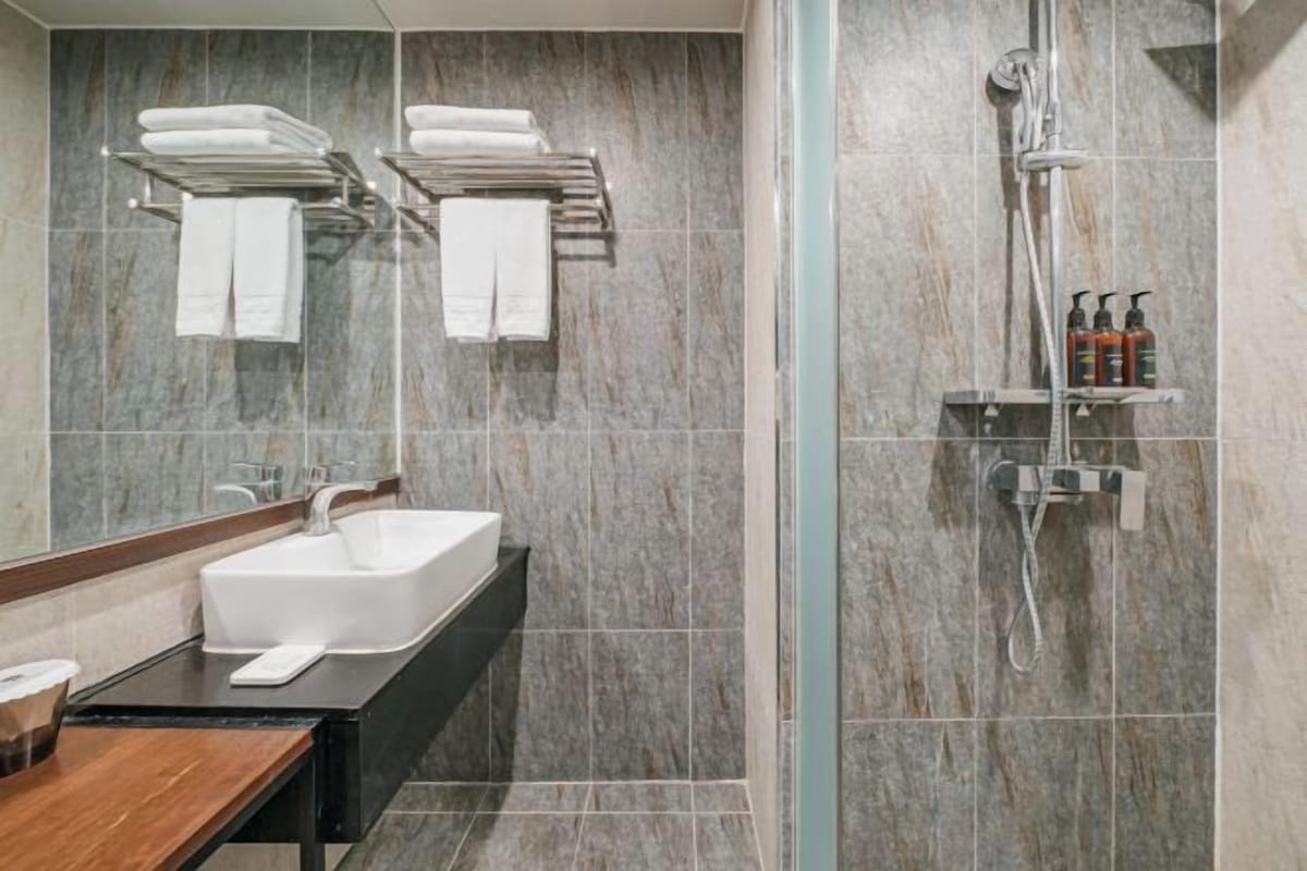 A modern bathroom with a marble wall, a white sink, a glass shower enclosure, and neatly arranged towels.
