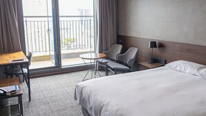 Une chambre d’hôtel comprenant un lit, un bureau avec un téléphone, deux chaises, une petite table et un balcon avec vue sur les bâtiments.