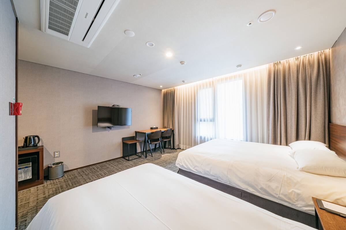 A hotel room with two beds, a desk, a chair, a television, and a window with curtains.
