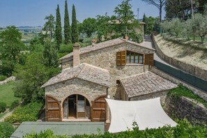 A stone house with a sloped roof, a central chimney, and a small attached structure with a window.