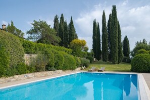 A swimming pool with two lounge chairs and a stone wall.