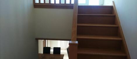 A wooden staircase with a handrail, leading to a lower level with a wooden table and chairs.