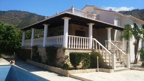 Ein zweistöckiges Haus mit Balkon, Schwimmbad und einer Bergkulisse.