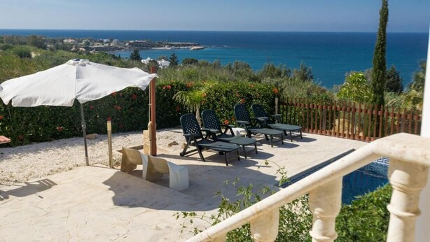 Eine Terrasse mit Sitzgelegenheiten im Freien, einem weißen Sonnenschirm und Blick aufs Meer.