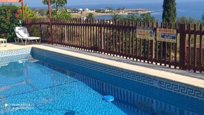 Una piscina con una valla de madera, un letrero de salvavidas y vista al mar.