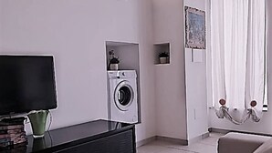 A modern living room with a flat-screen TV, a washing machine, a sofa, and a window with curtains. - Holiday Home 10 Minutes From Porto Cesareo (San Pancrazio Salentino)