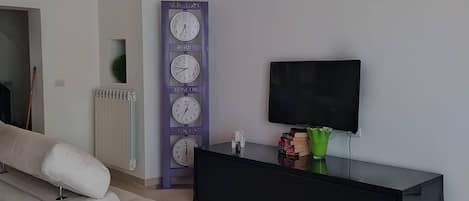 A modern living room with a sofa, a black entertainment unit, a flat-screen TV, and a wall clock with city names.