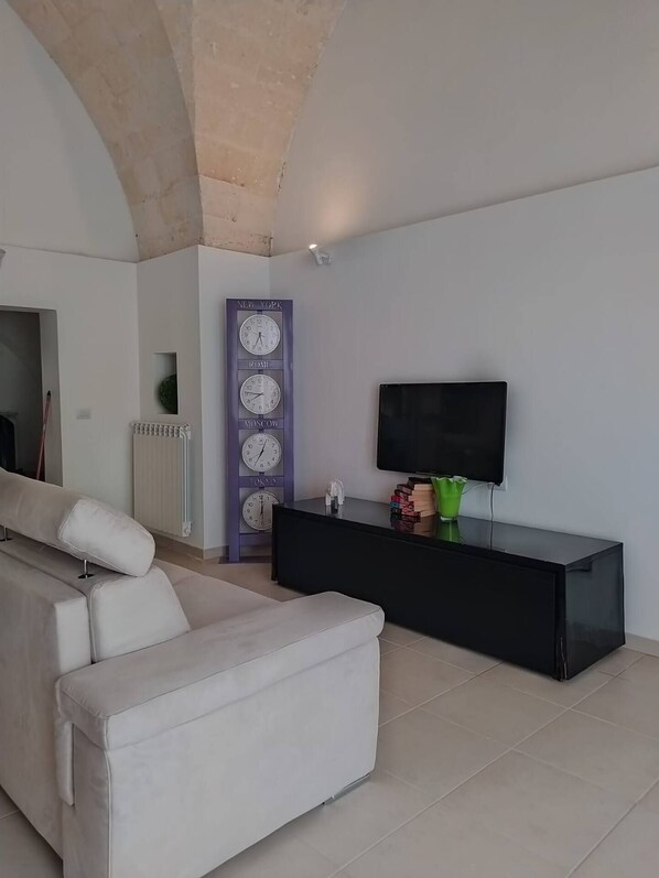 A modern living room with a sofa, a black entertainment unit, a flat-screen TV, and a wall clock with city names.