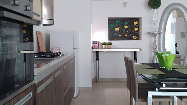 A modern kitchen with a built-in oven, a dining area with a table and chairs, and a decorative wall art piece. - Holiday Home 10 Minutes From Porto Cesareo (San Pancrazio Salentino)
