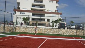 En tennisbana med en stenmur och en hög byggnad i bakgrunden.