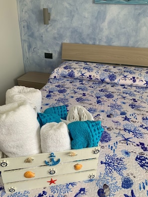 Coastal-inspired decor features a neatly made bed with a marine life-patterned bedspread and a nautical-themed chest of drawers.