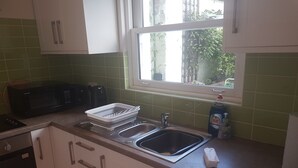 A kitchen with a double sink, a microwave, and a dish rack. - Lovely Large Garden Flat (Royal Tunbridge Wells)
