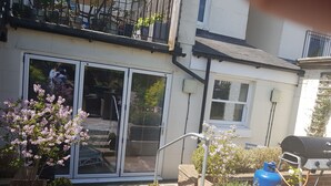 A residential backyard with a sliding glass door, potted plants, a barbecue grill, and a blue propane tank. - Lovely Large Garden Flat (Royal Tunbridge Wells)
