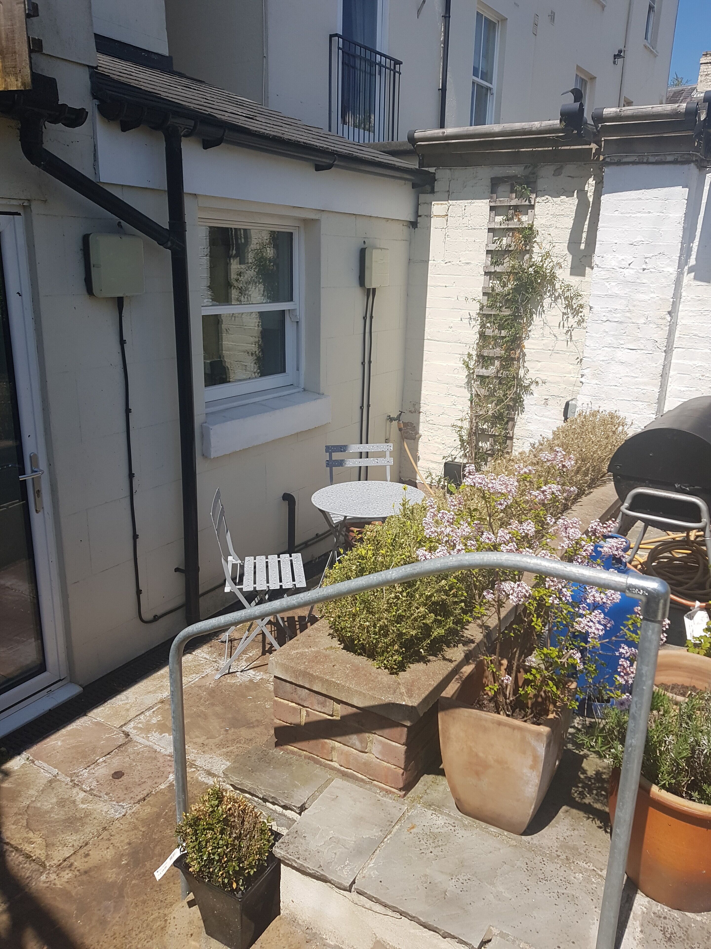 A residential patio with a white door, a small table, a chair, and potted plants.