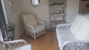 A room with a wicker chair, a white sofa, a mirrored wall, and a shelf with plants. - Lovely Large Garden Flat (Royal Tunbridge Wells)