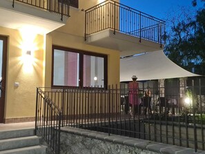 Un immeuble à plusieurs étages doté d’un balcon, d’un escalier et d’un espace extérieur couvert aménagé avec des tables et des chaises.