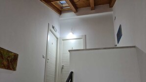 Un escalier avec un plafond en bois et des murs blancs, menant à une porte portant le numéro 5.