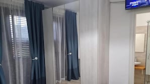 Une chambre à coucher moderne avec un lit, une armoire dotée de miroirs, un téléviseur et une petite enceinte noire.