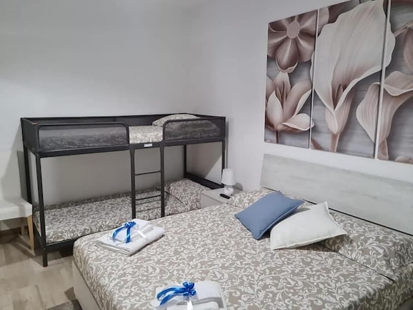 A bunk bed with a ladder, a bedside table with a lamp, and a bed with patterned bedding and pillows.