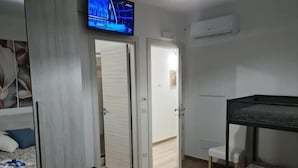 Une chambre d’hôtel avec un lit, une petite table, un téléviseur fixé au mur et une porte donnant sur une autre pièce.