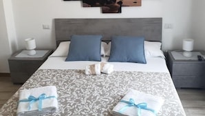 Ein ordentlich bezogenes Bett mit einem gemusterten Überwurf, zwei Kissen und zwei gefaltete Handtücher mit blauen Bändern.