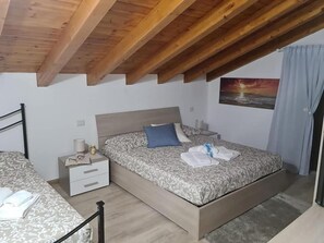 Une chambre avec un plafond en bois, un lit avec une literie à motifs, une table de chevet et un tableau accroché au mur.