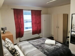 A bedroom with a bed, a nightstand, a wardrobe, and a window with curtains.