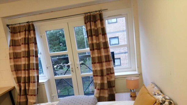 Ein Schlafzimmer mit Bett, Vorhängen, einem Fenster und einer Lampe.