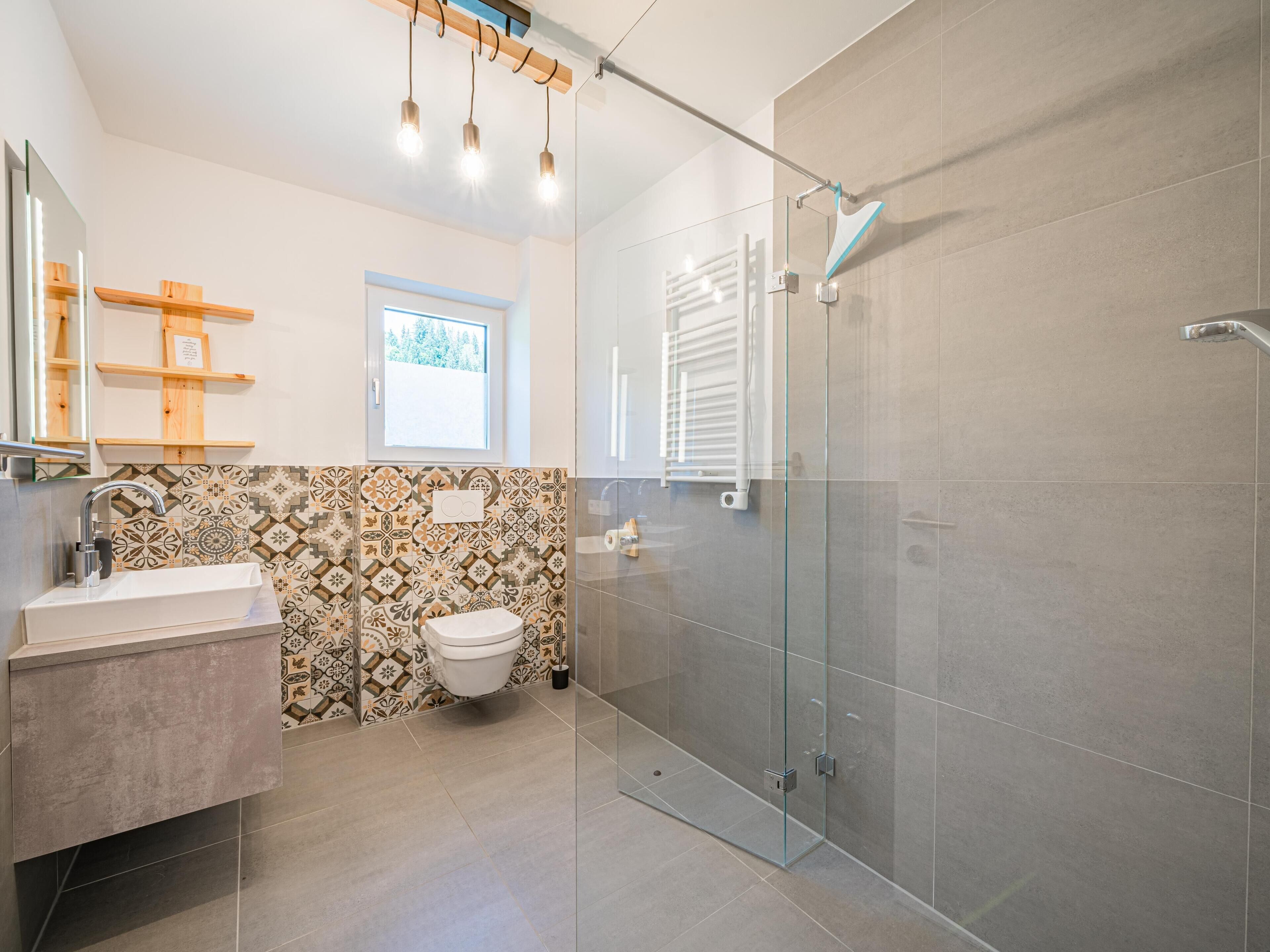 Ein modernes Badezimmer mit einer Duschkabine aus Glas, einem Waschbecken mit Spiegel und Wandfliesen mit Muster.