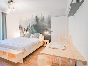 A bedroom with a bed, bedside tables, a wooden desk, and a wall mural of a forest.