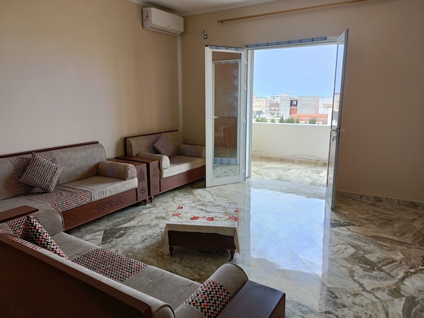 A living room with a sofa set, a coffee table, and a sliding glass door leading to a balcony.
