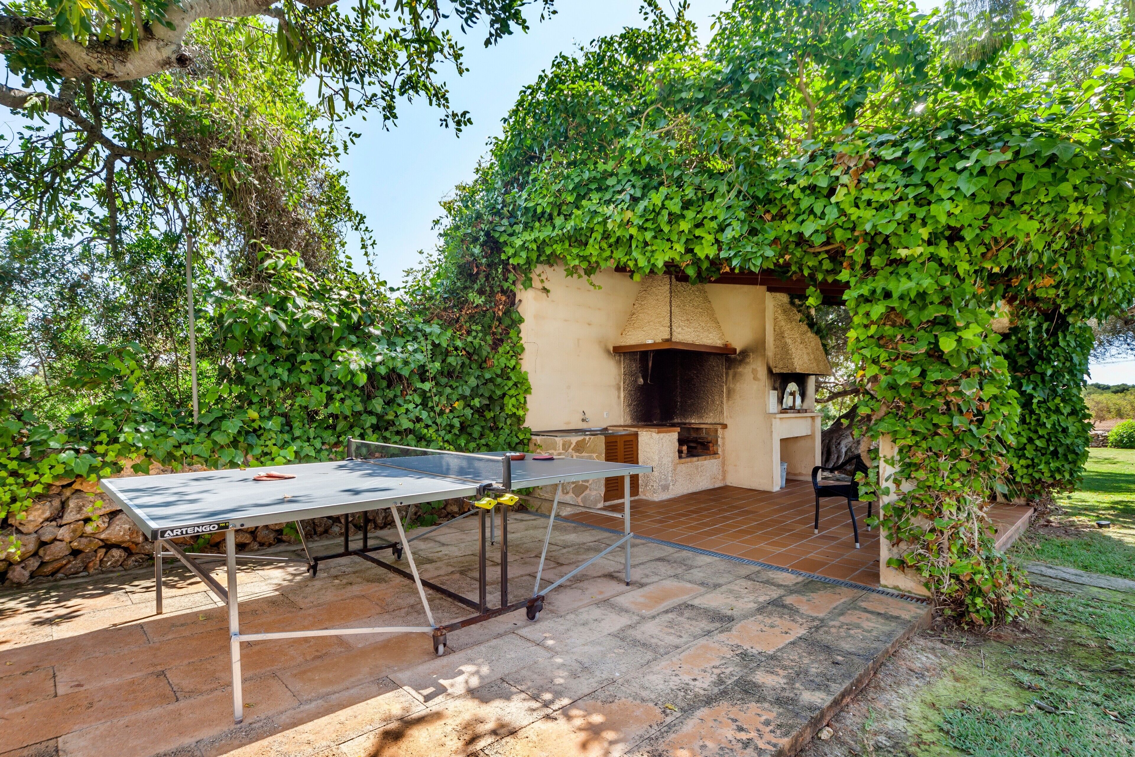 En udendørs terrasse med et pingpongbord, en stenspejs og en stenvæg.